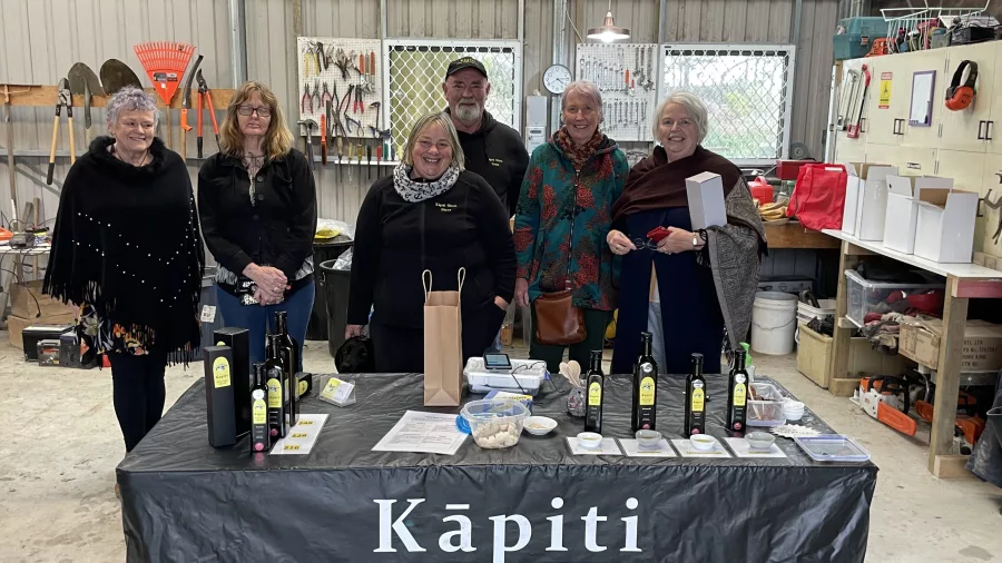Group of visitors and hosts standing behind a Kāpiti Olive Oil tasting table with products on display