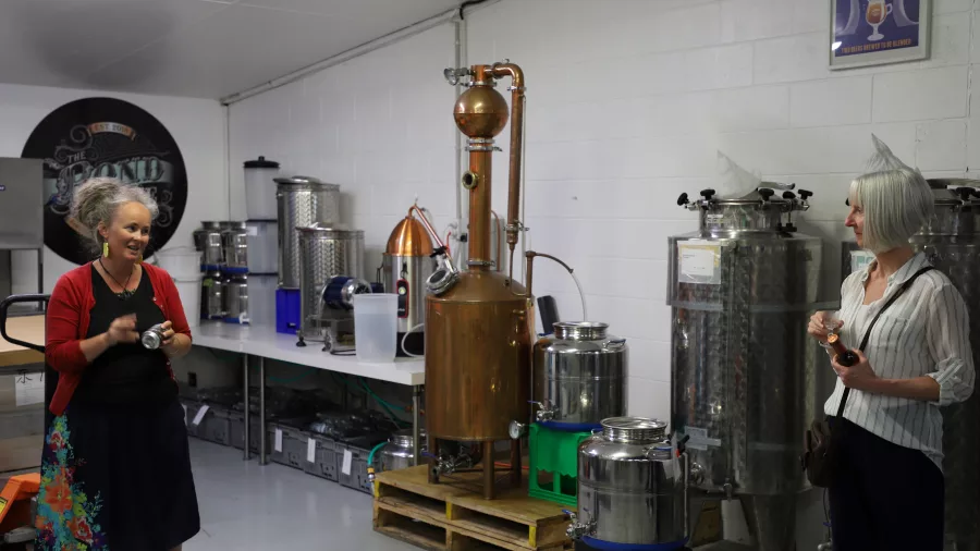 Two women talking during a distillery tour at The Bond Store in Kāpiti surrounded by brewing equipment