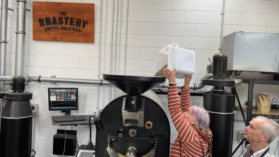 Woman pouring raw coffee beans into a roasting machine at The Roastery in Kāpiti