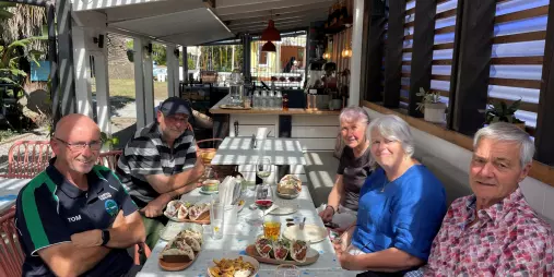 Group enjoying lunch and drinks at Hey Coastie in Waikanae Beach under a sunlit pergola