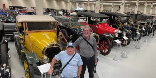 Two visitors posing in front of a yellow vintage car at Southward Car Museum in Paraparaumu