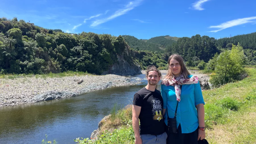 Two travellers posing by the River Anduin filming location in Wellington, surrounded by native bush and clear blue skies