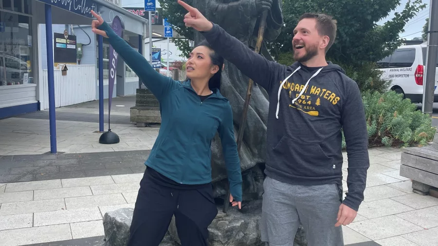 Two visitors posing playfully with the Gandalf statue outside Roxy Theatre in Miramar, Wellington, New Zealand