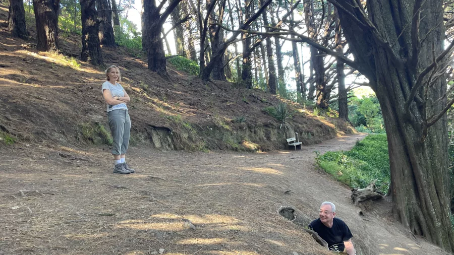 Man recreating the hiding scene from Lord of the Rings at Hobbits’ Hideaway while woman stands nearby on the forest trail