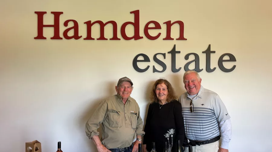 Three people posing in front of the Hamden Estate sign with wine bottles on the counter