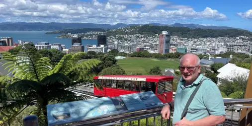 Smiling man at the Wellington Cable Car lookout with panoramic views of the city skyline and harbour