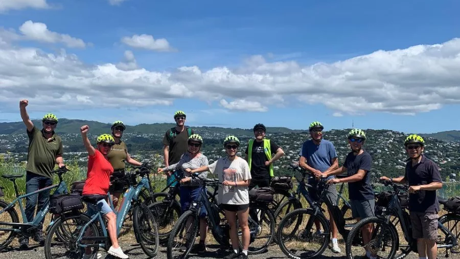 Cycling group posing with electric bikes at a lookout on a sunny day in Wellington