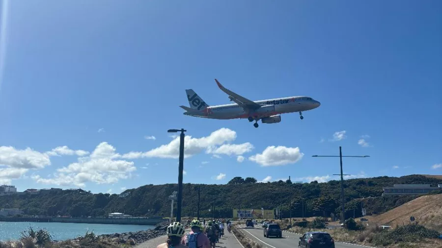 Cyclists riding along a coastal path as a plane descends near Wellington Airport