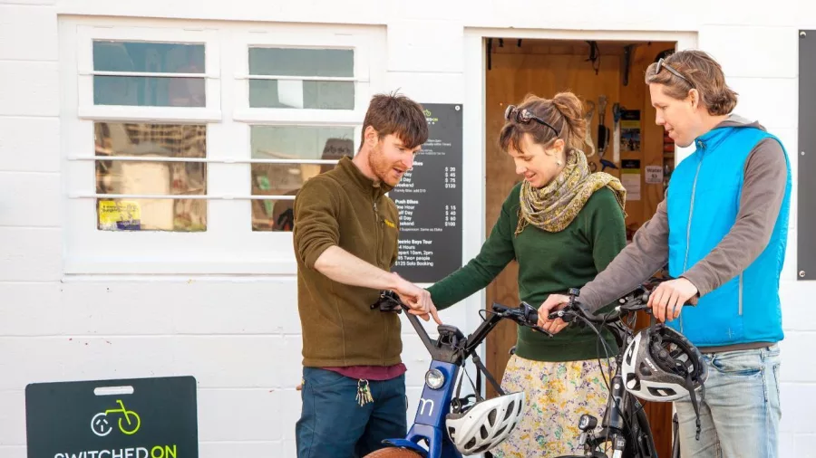 Two customers receiving a bike setup from staff outside Switched On Bikes shop in Wellington