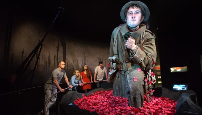 Visitors standing in front of a giant sculpture of a soldier surrounded by red rose petals at Te Papa museum.