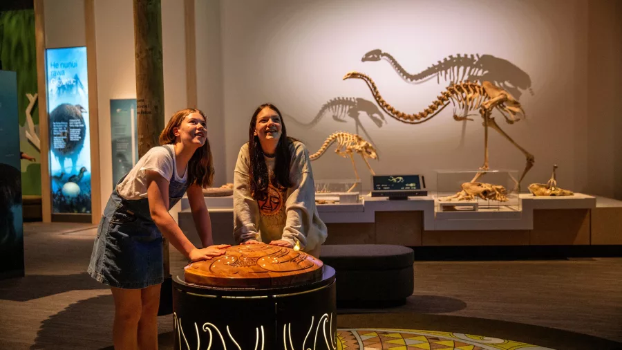 Two girls interacting with a hands-on display at Te Papa’s natural history exhibit, moa skeletons in background