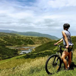 Woman on an e-bike overlooking Pencarrow Lakes surrounded by green hills in Wellington