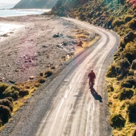 Cyclist riding solo along the sunlit Pencarrow Coast Road in Wellington with ocean views