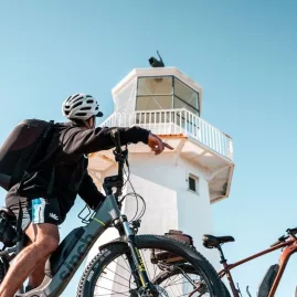 Cyclist pointing at Pencarrow Lighthouse in Wellington with eBikes parked nearby