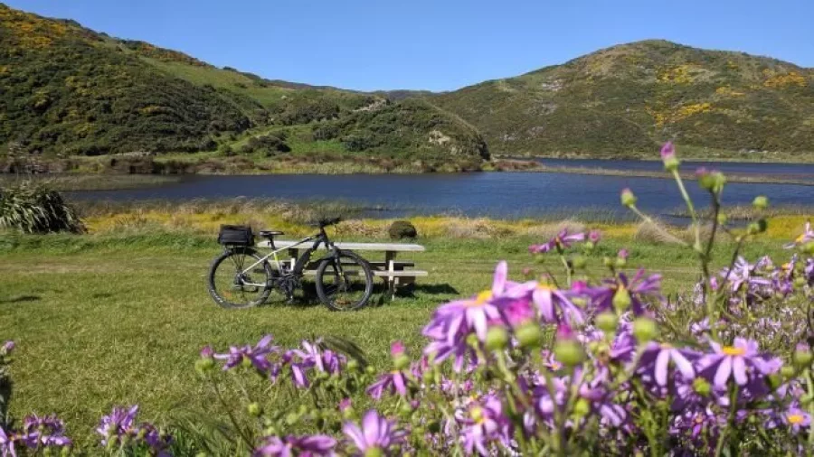 Picnic table with eBike near Pencarrow Lakes surrounded by hills and wildflowers
