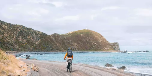 Cyclist riding along the coastal trail towards Pencarrow Lighthouse near Wellington, New Zealand