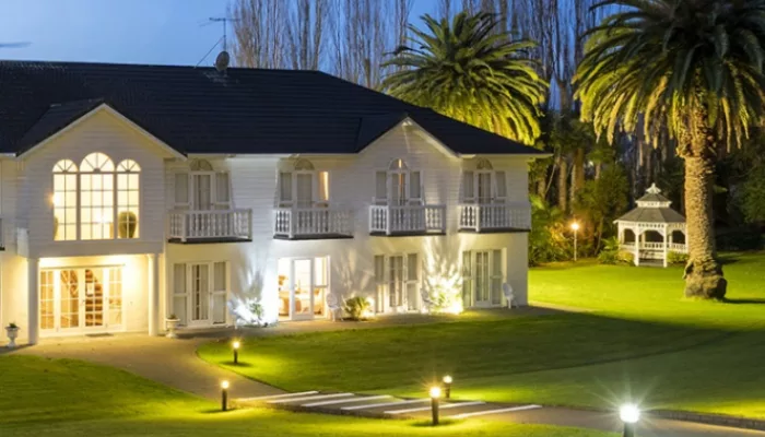 Wallaceville Country Hotel lit up at dusk in Upper Hutt surrounded by palm trees and garden paths