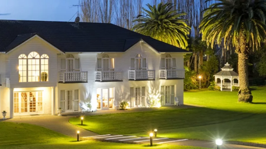 Wallaceville Country Hotel lit up at dusk in Upper Hutt surrounded by palm trees and garden paths