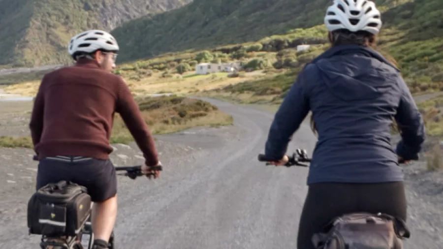 Couple cycling along the Wild Coast section of the Remutaka Cycle Trail with dramatic mountains in the background