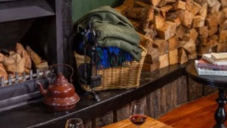 Cosy fireplace at Brac & Bow with wine glasses and wood stack at The Royal Hotel Martinborough