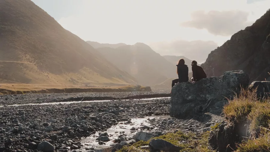 Two cyclists resting on a rock by the Wild Coast riverbed in Wairarapa