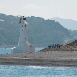 Group of cyclists near Pencarrow Lighthouse with Wellington hills in the background