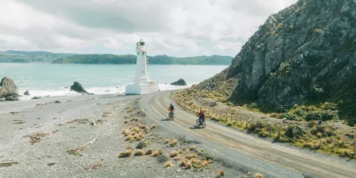 Cyclists riding towards Pencarrow Lighthouse along the rugged Wellington coastline in New Zealand