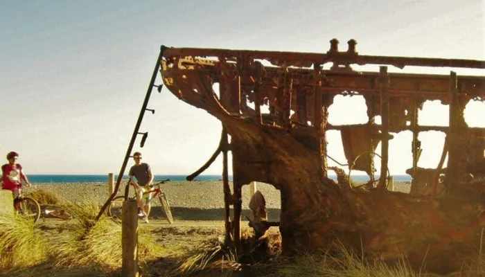 Cyclists stop beside the rusted SS Paiaka shipwreck on Pencarrow Coast in Wellington