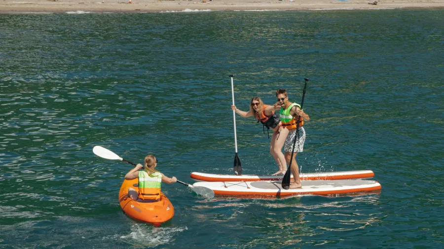Two people on stand-up paddleboards and one person kayaking at Days Bay with the beach and buildings in the background