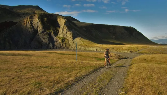 Cyclist biking along a rugged trail with dramatic cliffs on the Remutaka Cycle Trail