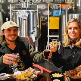 Couple toasting with beers in front of fermenters during a craft beer tour in Wellington