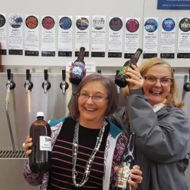 Two women smiling and holding craft beer bottles at a taproom during a Wellington brewery tour