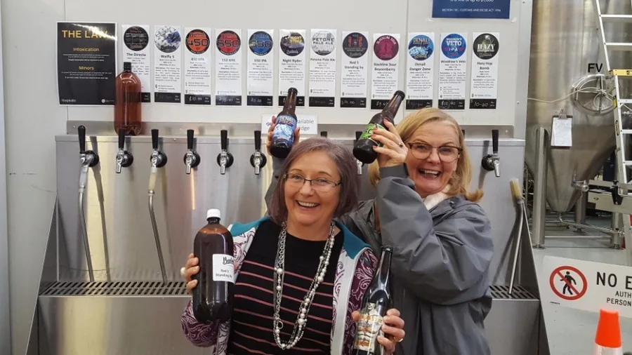 Two women smiling and holding craft beer bottles at a taproom during a Wellington brewery tour