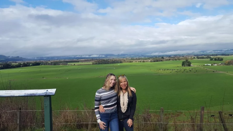 Two women posing in front of a wide green farmland view in Martinborough