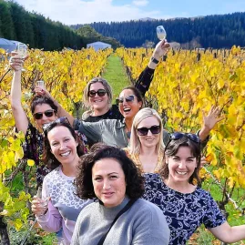 Group of women enjoying wine in a vineyard with golden autumn leaves in Martinborough