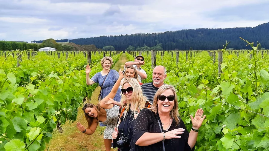 Group of travellers smiling and posing between vineyard rows in Martinborough