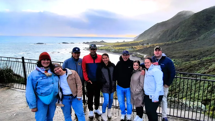 Group of travellers posing by the coast near Wellington with sea cliffs and sunset
