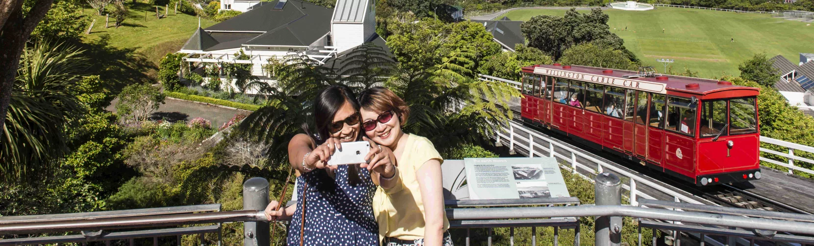 Two women taking a selfie at the top of the Wellington Cable Car with city and harbour in the background