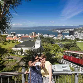 Two women taking a selfie at the top of the Wellington Cable Car with city and harbour in the background