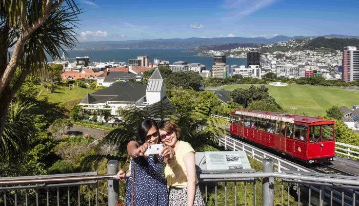 Two women taking a selfie at the top of the Wellington Cable Car with city and harbour in the background