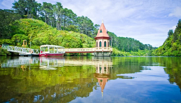 Zealandia reservoir tower and electric boat reflected in forest-lined lake in Wellington