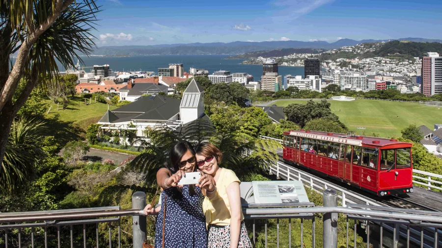 Two women taking a selfie at the top of the Wellington Cable Car with city and harbour in the background