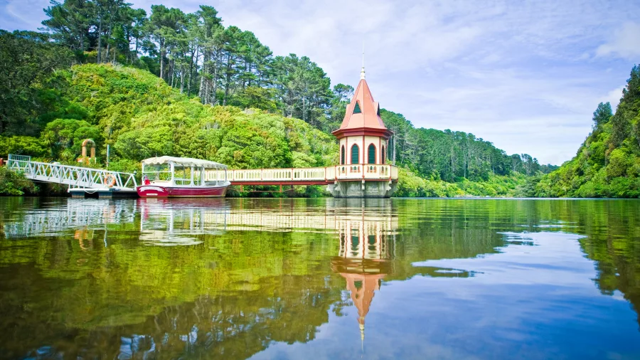 Zealandia reservoir tower and electric boat reflected in forest-lined lake in Wellington