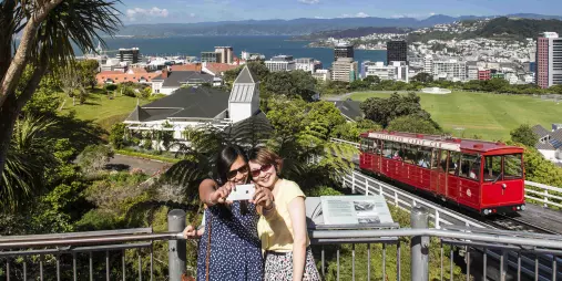 Two women taking a selfie at the top of the Wellington Cable Car with city and harbour in the background