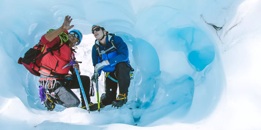 Guide and hiker pause inside an ice cave during the Extreme Fox All Day Heli Hike.
