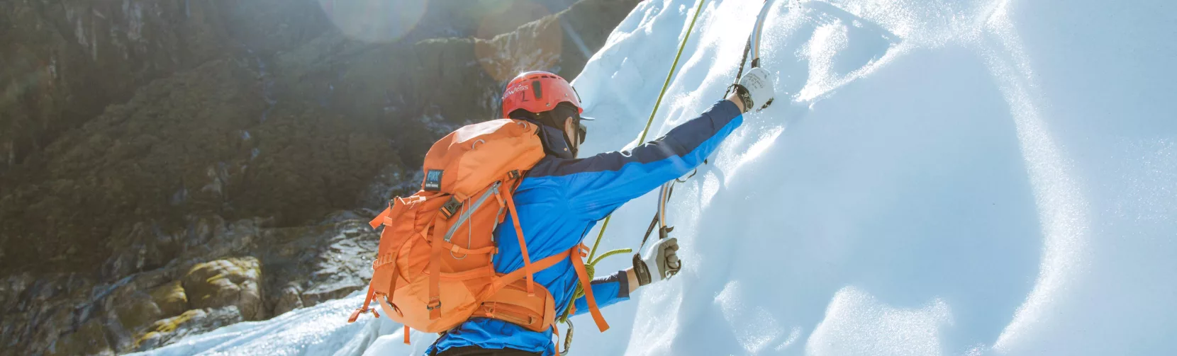 A climber uses ice axes to scale a frozen wall on Fox Glacier in bright alpine light.
