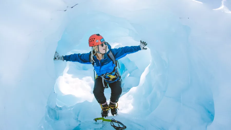 Adventurer poses inside a stunning blue ice tunnel on the Fox Glacier Heli Hike.