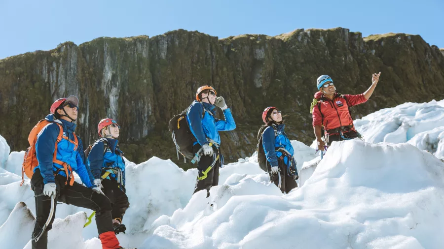 Group stands on glacial ice as their guide points out key landmarks and terrain.