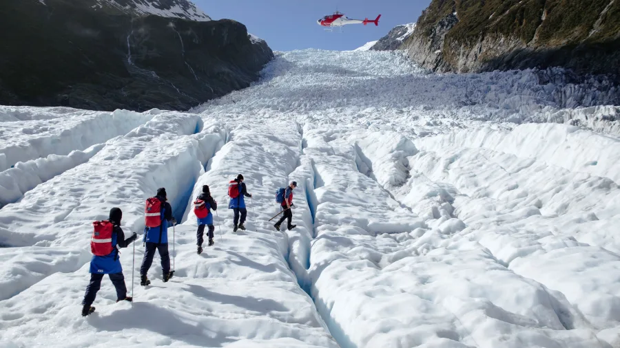 Helicopter flies above hikers after drop-off on Fox Glacier for an all-day hike.