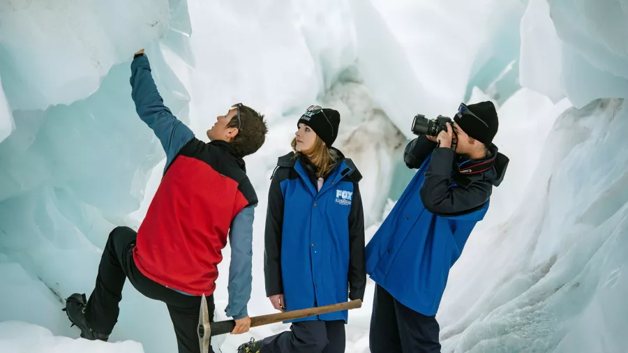 Fox Glacier guide explains ice formations inside a narrow glacial cave to curious hikers.